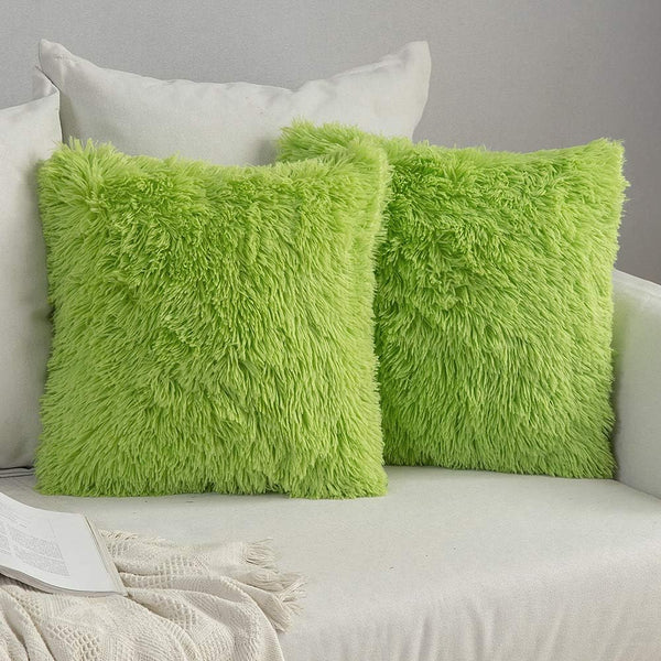 Two green fluffy pillows on a sofa against a gray wall.