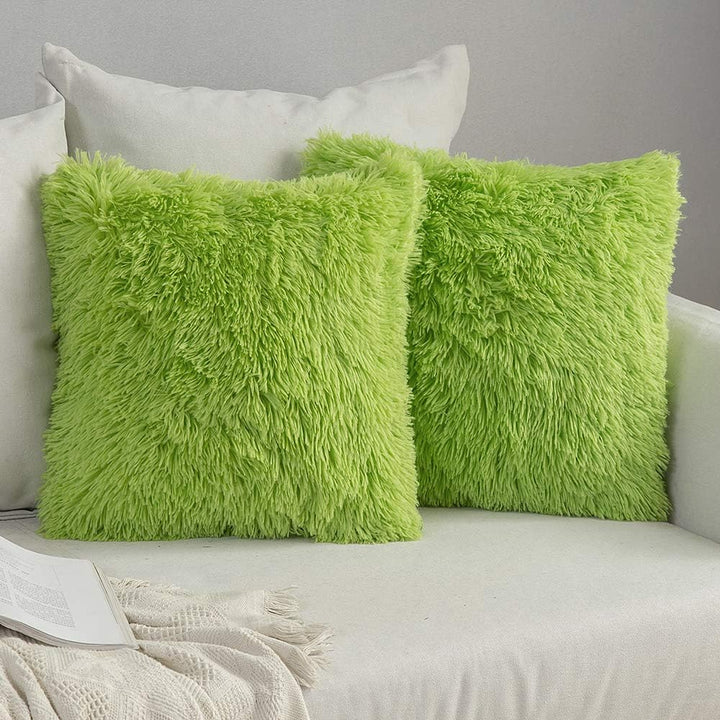 Two green fluffy pillows on a sofa against a gray wall.