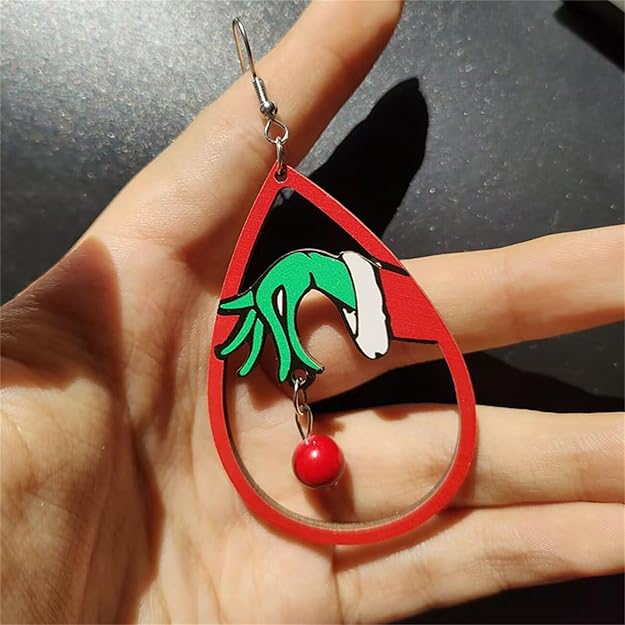Earring with green hand, white hat, and red ball design held in a hand against a dark background