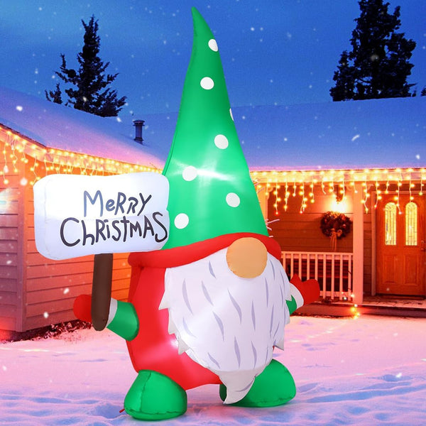 Inflatable gnome with a 'Merry Christmas' sign in front of a house decorated for Christmas.