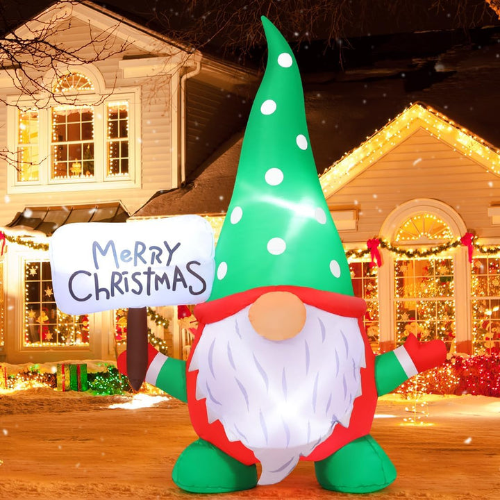 Inflatable Christmas gnome holding a 'Merry Christmas' sign in front of a decorated house.