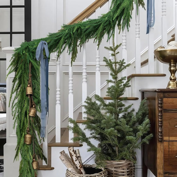 Decorative green garland with bells and ribbons on a staircase with a small tree and wooden cabinet.