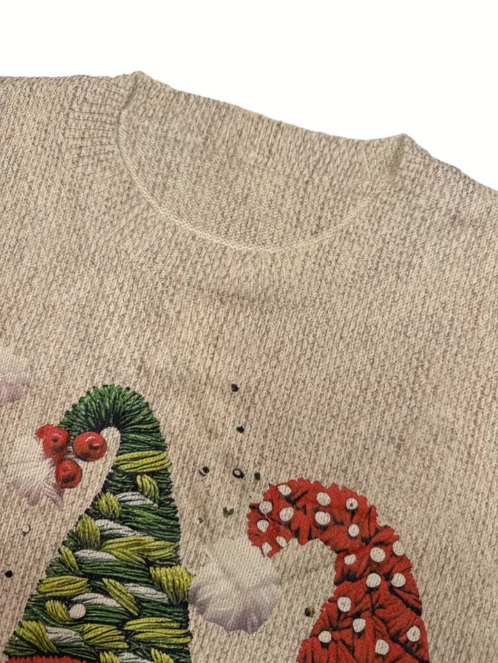 Close-up of a beige sweater with embroidered Christmas-themed design.