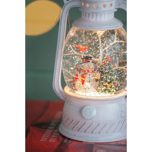 Decorative lantern with a snow globe containing a snowman and lights, on a red surface.